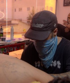 Degusta tatuando de máscara e boné